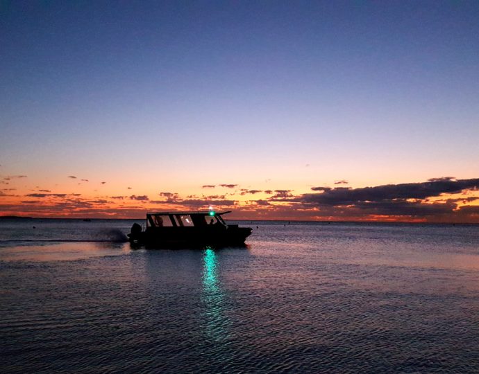 un bateau sur l'eau à la tombée de la nuit avec un coucher du soleil orange