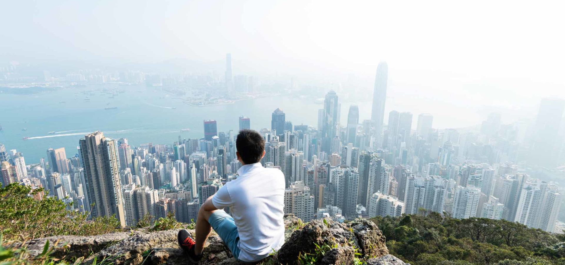 Men sitting on the top of mountain and looking cityscape.
