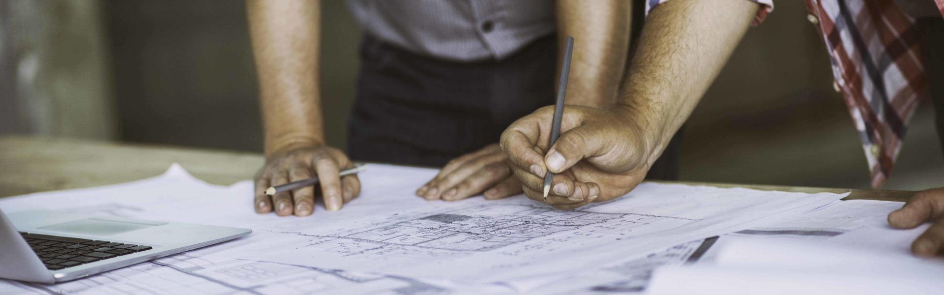 Close up of two architect's hands holding pencils over some building blueprints.